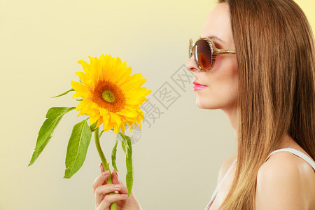 更近的一面观察着迷人的夏日女子身着太阳镜手拿向日葵背黄色景图片