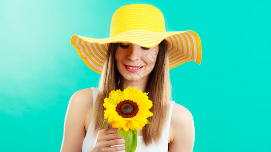 穿着黄帽子的有吸引力夏日女子肖像蓝色背景的向日葵手握着图片
