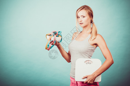 饮食健康饮食瘦身理念健身女孩拿着碗碗里有许多彩色的卷尺作为节食的标志和体重秤工作室拍摄于蓝色图片