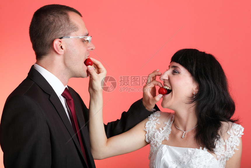 快乐笑的新娘和郎快乐的年轻情侣玩耍地吃红底的稻草图片