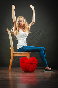 心碎的爱概念坐在椅子上的悲伤忧郁女人坐在黑暗背景的地板上红心枕头图片