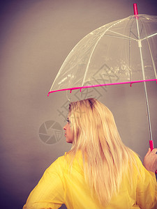 身穿黄色雨衣的金发女人拿着透明的雨伞检查天气是否下雨图片