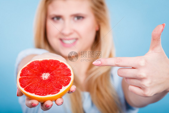 女微笑的孩手握着一半的红葡萄果柑橘水用手指着建议健康饮食在蓝色上饮食减肥概念女手握着葡萄果柑橘水图片