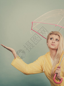 身穿黄色雨衣的金发女人拿着透明的雨伞检查天气是否下雨图片