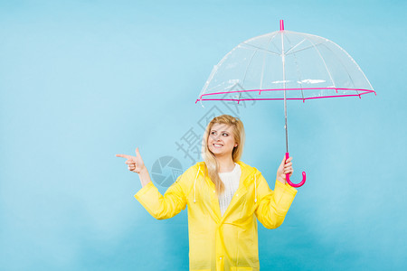 身穿黄色雨衣的金发女人拿着透明的雨伞检查天气是否下雨图片