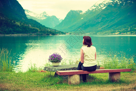 旅游概念在挪威SognogFjordane县Olden村坐在海边的长椅上观光年轻旅游妇女在海边观光的fjords美丽的风景图片