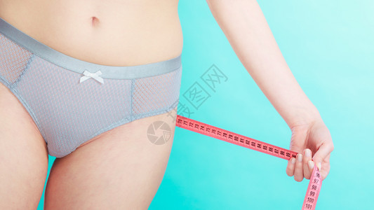 穿内衣用体积胶带测量臀部的瘦女孩体重减肥与蓝色相对用体积胶带测量臀部图片