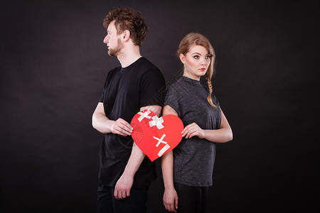 心碎难恋的概念伤心不幸福的夫妻男女手拿纸红心用石膏绷带固定关系