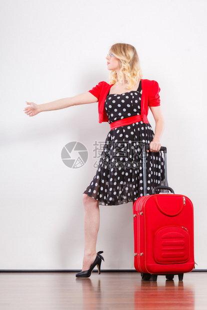 穿着Polka圆点黑裙子的美丽可爱女人准备搭便车旅行的红色手提箱举高穿着红色手提箱搭便车的女人图片