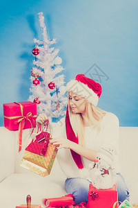 圣诞时间概念穿着圣达克萨斯帽子为圣诞节准备礼物坐在家中沙发上舒适的假日内地年轻金发女孩节快乐她们为圣诞节准备礼物图片