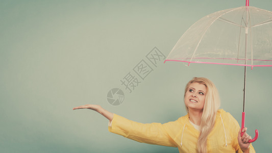 身穿黄色雨衣的金发女人拿着透明的雨伞检查天气是否下雨图片