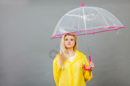 穿着黄色雨衣的无聊金发女人拿着透明的雨伞等待水图片