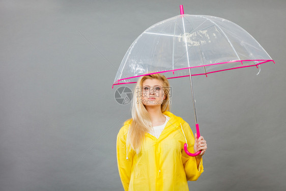 穿着黄色雨衣的无聊金发女人拿着透明的雨伞等待水图片