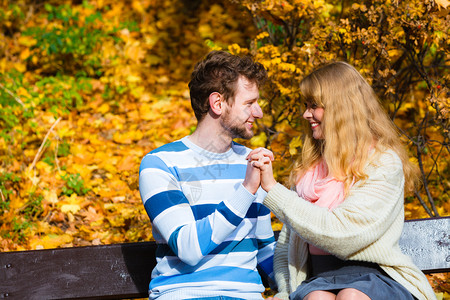 在阳光明媚的日子里年轻浪漫夫妇坐在秋天公园的长凳上拥抱在秋天公园的情侣们坐在长椅上图片