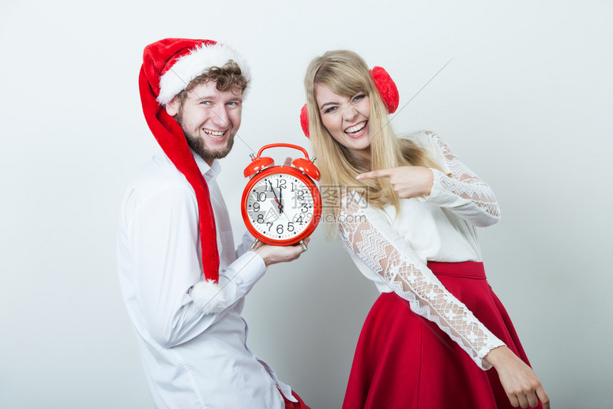 可爱的情侣拿着闹钟漂亮的女人戴着耳膜帅的男子戴着圣达克萨斯帽子圣诞季节概念快乐的情侣带着闹钟快乐的男女带着闹钟图片