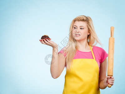 女人拿着蛋糕和滚动针穿着黄围裙女人拿着纸杯蛋糕和滚动针穿着围裙图片