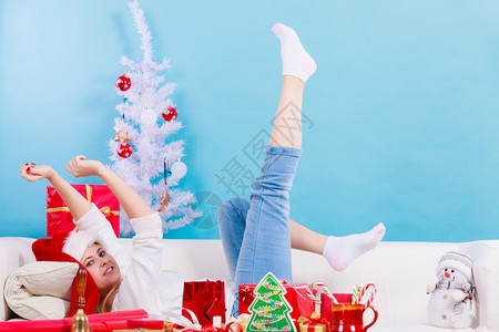 金发女人坐在沙上戴着圣诞帽子享受温暖的圣诞节气氛图片