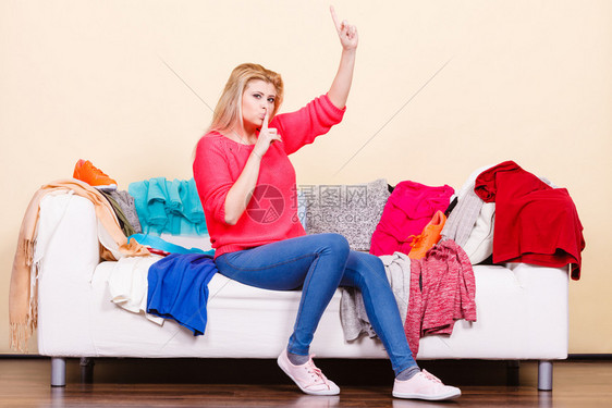 妇女不知道坐在乱七八糟的沙发上穿什么衣服着一叠表现出静默姿态妇女不知道坐在沙发上穿什么图片