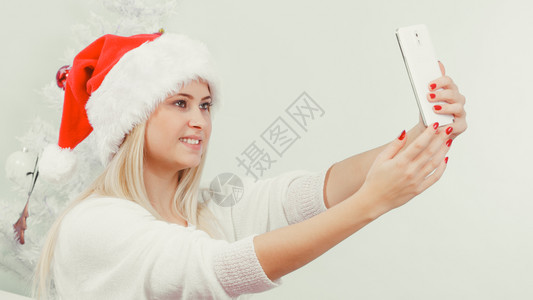 现代节日概念穿着圣诞礼帽的金发女人给自己拍圣诞照用智能手机自拍背景图片