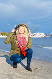 妇女穿着温暖的夹克在海边滩上放松阳光寒冷的一天图片