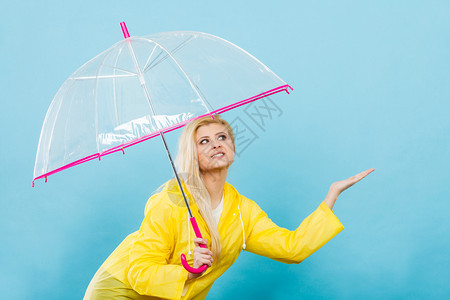 身穿黄色雨衣的金发女人拿着透明的雨伞检查天气是否下雨图片