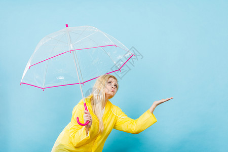 身穿黄色雨衣的金发女人拿着透明的雨伞检查天气是否下雨图片