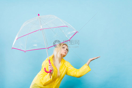 身穿黄色雨衣的金发女人拿着透明的雨伞检查天气是否下雨图片