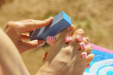 在海滩户外渡假期间无法辨认的妇女修脚指甲用分离器擦脚指甲图片