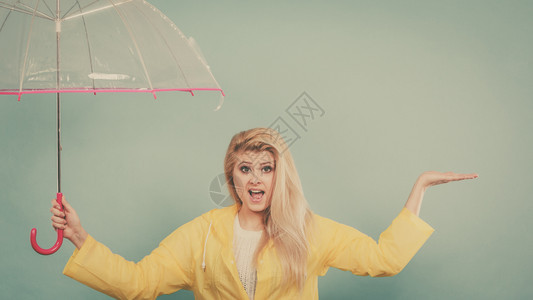 身穿黄色雨衣的金发女人拿着透明的雨伞检查天气是否下雨图片