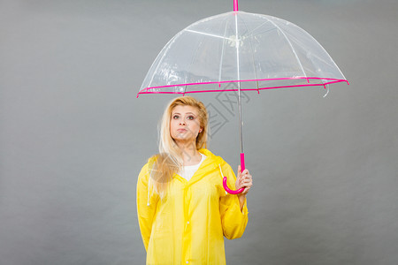 穿着黄色雨衣的无聊金发女人拿着透明的雨伞等待水图片