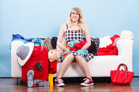 快乐的女士坐在沙发上准备度假选择衣服包装在手提箱里图片