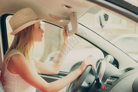 驾驶汽车时照镜子的年轻有吸引力女人图片
