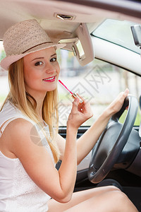 年轻有吸引力的在后视镜中照子的妇女在她嘴唇上画在驾驶汽车时涂化妆品图片
