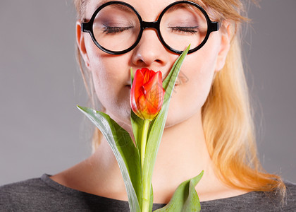 美丽的女孩闻着鲜花香味戴着眼镜的年轻快乐女人闻着红色的郁金香纳迪女孩闻着鲜花的香味图片