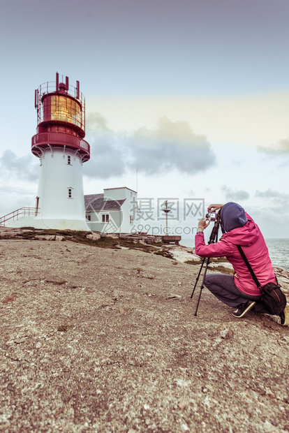 女旅游客行者在挪威南海岩石岸边缘历史红白灯塔拍照LindesnesFyr灯塔挪威林德森灯塔旅游者图片