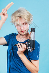 时尚和风格年轻时尚的男发型师理有变化外观的新念金发男子手持吹机和梳子在蓝色上制造新的发型戴吹机的特伦迪男子图片