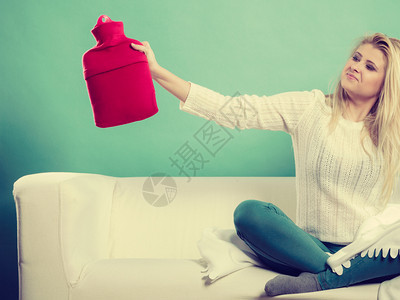 在寒冷的冬季或秋天变暖妇女坐在沙发上拿着热水瓶图片