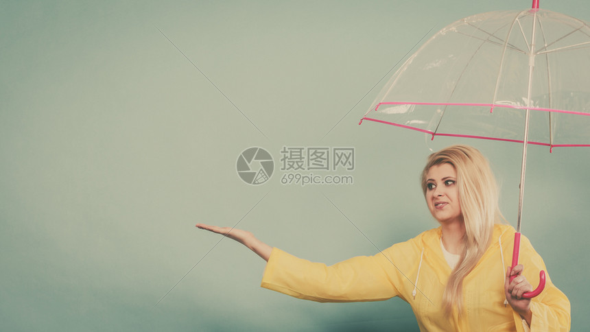 身穿黄色雨衣的金发女人拿着透明的雨伞检查天气是否下雨图片