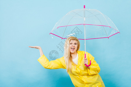 身穿黄色雨衣的金发女人拿着透明的雨伞检查天气是否下雨图片