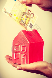 家庭储蓄和财政经济概念男人把欧元钱放进像房子一样的小猪银行工作室拍的灰色背景男人把钱放进家庭小猪银行图片
