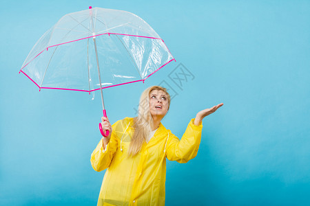 身穿黄色雨衣的金发女人拿着透明的雨伞检查天气是否下雨图片