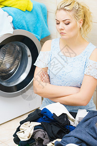 身处一堆大衣物的不幸女坐在洗衣机旁边做着疲劳的家务图片