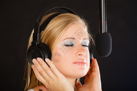 音乐激情舞台恐惧概念金发年轻女子唱着麦克风头戴大耳机在工作室表演歌曲图片