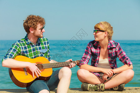 年轻男人在海边的户外和女友玩吉他约会情侣图片