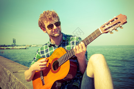 快乐的年轻人在海边弹吉他戴墨镜的帅哥放暑假放松年轻人在海边弹吉他背景图片