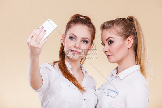 姐妹或最好的朋友两个金发女学生用智能手机相自拍照玩得开心图片