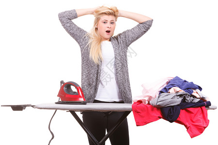 干家务照顾庭概念疲劳的打哈女人站在板后用一堆衣服熨铁疲劳的打哈同时熨铁疲劳的打背景图片