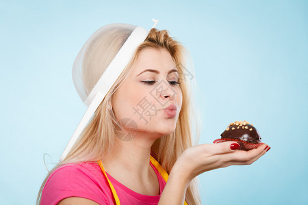 在家烘焙美味的甜点和糖果的概念一个女人拿着美味的甜巧克力蛋糕围裙戴着香炉头上戴着帽子拿着纸杯蛋糕头上戴着香炉的女人图片