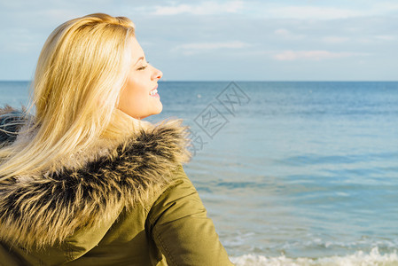 妇女穿着温暖的外套在海边沙滩阳光寒冷的天气后视海滩上的放松寒冷天气图片