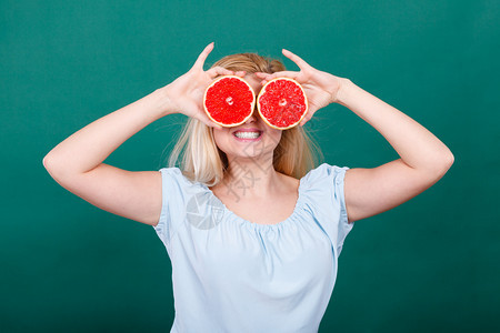 金发女少手握着两半红葡萄果柑橘水蒙着眼睛看绿色健康饮食营养幸福快乐概念女孩用葡萄果遮住眼睛图片